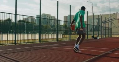 African american handsome man wears sportswear plays basketball does slam dunk ties to score winning points during game with friends outdoors at playground .