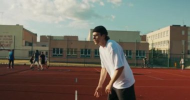 Young man hipster wearing sportswear plays basketball at playground court with friends delighted guy shows skill tries to make slam dunk trains outside.
