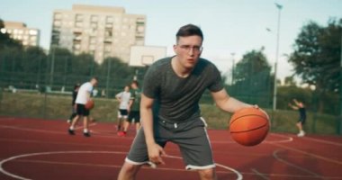 Slow motion selective focus concentrated man in fashionable sportswear and glasses plays basketball at pplayground shows skills scores winning points does slam dunk .