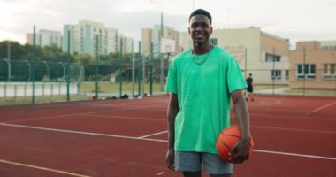 Portrait of delighted african american young basketball player holding ball in hands standing outside at playground shoting process during game.