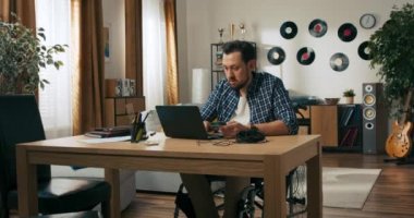 Tekerlekli sandalyedeki sakallı adam evde internetten çalışıyor. Mutlu adam serbest meslek kavramını tamamladı. Bilgisayarı kapatan kişi kredi kartına kolayca ödeme yapıyor..