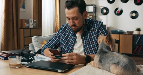잘생긴 청년은 셔츠를 테이블에 행복하게 강아지 강아지와 온라인 카드를 — 비디오