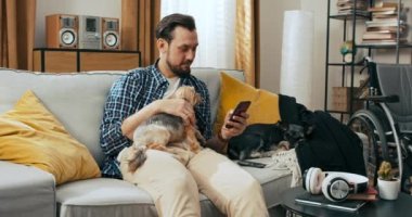 Mutlu yakışıklı sakallı adam hafta sonları köpeğiyle otururken elinde cep telefonuyla mesajlaşarak sohbet ediyor. Tekerlekli sandalyesi olan engelli.