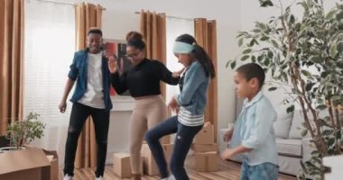 Mutlu bir aile oturma odasının ortasında dans eder, genç ebeveynler ve çocukları yeni bir daireye taşınmayı kutlarlar, birlikte sevinirler, koreografi çalışırlar.