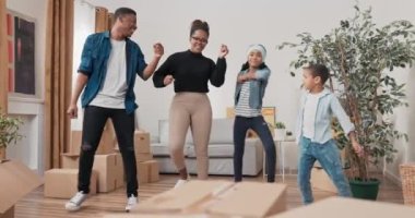 Mutlu bir aile oturma odasının ortasında dans eder, genç ebeveynler ve çocukları yeni bir daireye taşınmayı kutlarlar, birlikte sevinirler, koreografi çalışırlar.