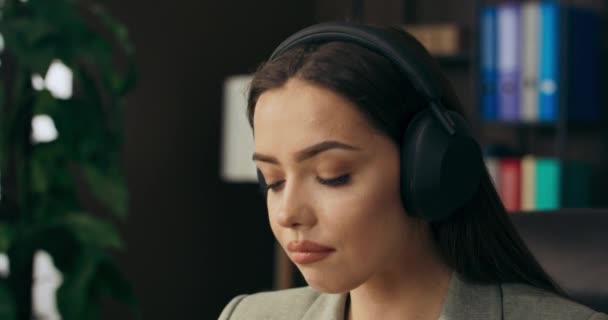 放松冷静的女人坐在桌旁放松地听音乐 带着无线耳机在网上谈论梦寐以求的工作 — 图库视频影像