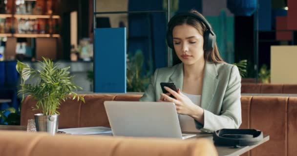 Young Woman Restaurant Listens Music Wearing Wireless Headphones Working Laptop — Stock Video