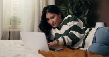Yatak odasında uzanan güzel bir kadın egzotik ülkelere seyahat satın alıyor, online seyahat acentası kullanıyor, rezerve edilebilir otel kullanıyor, tatilini kredi kartıyla ödüyor..