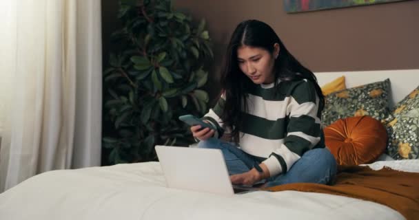 这位颇受欢迎的博主坐在卧室的床上 从家里开始工作 这个女孩通过电话和笔记本电脑在她的社交网络上增加了职位 — 图库视频影像