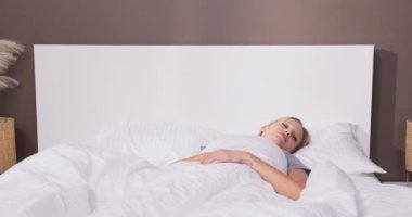 Bir kadın sabah yataktan kalkıyor ve yorganı üzerinde oturuyor. Bir gece uyuduktan sonra boyunda ağrı, rahatsız bir uyku pozisyonu, ağrıyan bir boyun..