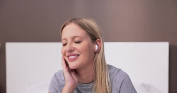 Молода Блондинка Сидить Ліжку Спальні Піжамі Слухає Музику Бездротових Навушниках — стокове відео