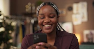 Oturma odasındaki Afrikalı bir kadın başarılı online işini cep telefonuyla yürütüyor. Kendini başarılı ve tatmin olmuş hissediyor..