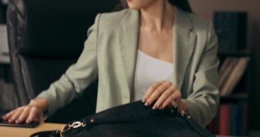 Yakın çekim işçisi kadın farklı eşyaları çantaya koyuyor, işi bitiriyor ve yoğun bir iş gününden sonra eve gidiyor. Bayan kulaklık takıyor ve takım elbise giyiyor. .