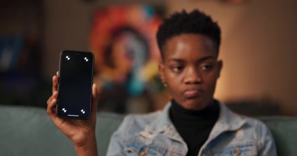 Afrikanerin Präsentiert Handy Mit Dunklem Bildschirm Wohnzimmer Und Diskutiert Über — Stockvideo