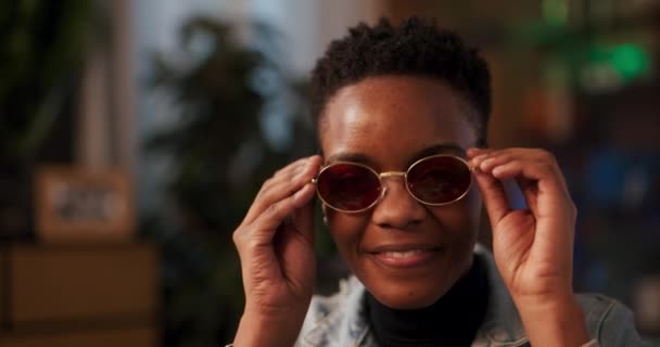 写真はピンクのサングラスをかけたアフリカ人女性の魅力を捉え カメラが生き生きとしたポジティブな視線に自信を持って笑顔を放射し 親しみやすい性格を示唆している — ストック動画