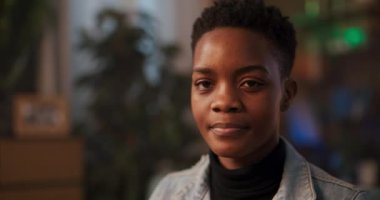 Kısa saçlı Afrikalı bir kadın, parlak bir gülümsemeyle kameraya doğru dönüyor, mutluluk ve memnuniyet hissi yayıyor, neşeli ve neşeli bir kişiliğe sahip olduğunu gösteriyor..