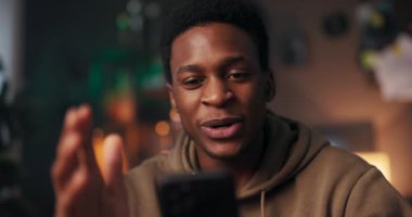 Bir koltuğun üzerindeki Afrikalı Uzun Mesafeli İlişki katılımcısı bir cep telefonu tutuyor, video görüşmesi sırasında olumlu duygular gösteriyor ve uzun mesafeli bir ilişkiyi besliyor..