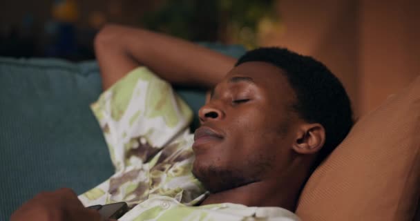 疲惫的非洲人躺在客厅的沙发上 从忙碌的一天中恢复过来 他猛然醒来 伸出手去拿起手机 急于想知道他家乡的最新消息 — 图库视频影像