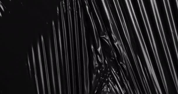 細長いセロハンラップの彫刻的傑作のように展開し 深い黒を背景にした伸縮性のあるプラスチックフィルムカスケードとして特別な触覚体験に身を浸します — ストック動画