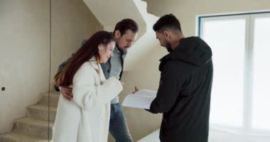 Emlakçı, ev almakla ilgilenen aileyle birlikte daireyi ziyaret ederek iç tasarım planını tartışıyor..