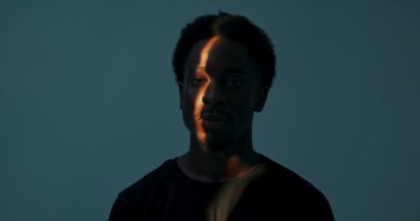 Soyut kavram. Afro-Amerikan esmer tenli adam yan tarafa bakıyor doğrudan kameraya bakıyor ve karanlık stüdyoda ışığı yakalıyor..