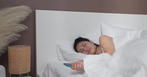 一个女人睡在铺着白布的床上 女孩们的睡眠被电话上的闹钟打断了 闹钟响了 她伸手去拿 然后用被子盖住自己 打起瞌睡 — 图库视频影像