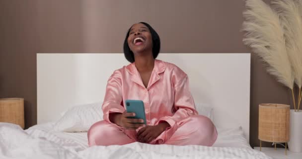 一个年轻的女人坐在床上看滑稽的电话录像 醒来时使用智能手机的概念 — 图库视频影像