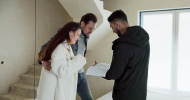 Emlakçı, ev almakla ilgilenen aileyle birlikte daireyi ziyaret ederek iç tasarım planını tartışıyor..