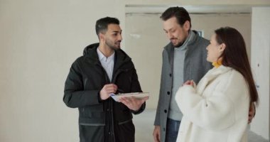 Bir emlakçı genç bir çifte çoklu aile evi satıyor. Adam sözleşmenin şartlarını açıklıyor ve imza için yerine kalemle işaret ediyor. Kadın cesurca baş harflerini.