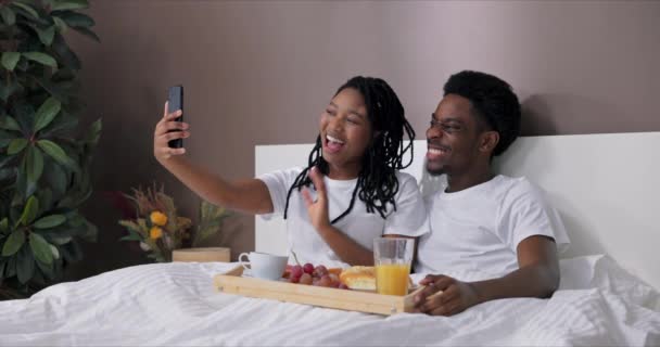 新婚夫妇度蜜月时快乐而快乐 快乐可爱的黑皮肤妻子拿着手机 带着家人的视频电话 向大家展示可爱丈夫的早餐 高兴地在镜头前挥手 — 图库视频影像