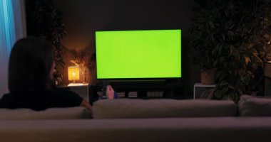 Genç bir kadın sıcak oturma odasında kanepede oturup televizyon seyrediyor. Uzun bir iş gününün ardından ev yapımı yeşil ekranda dinleniyor..