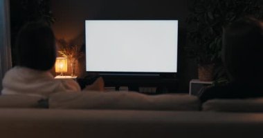 İki arkadaş son dedikoduların hafta sonu konseptini konuşuyor. Oturma odasında oturan mutlu kadınlar TV haber filmi beyaz ekran maket televizyon izliyorlar rahat oturma odasında, omuzlarının üstünde..