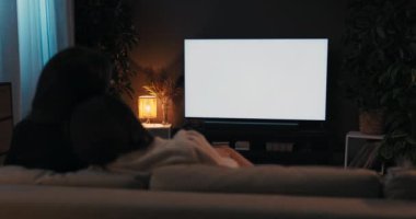 Mutlu genç kızlar gecesi. İki arkadaş oturma odasında kanepede oturmuş, dinleniyor, televizyon seyrediyor, evinde beyaz ekran maketi var..