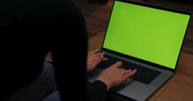 Bilgisayarın başında oturan yeşil ekran maketi olan bir kadın. Oturma odasındaki rahat koltuğunda oturmuş yazı yazıyor. Omzunun üstünden..