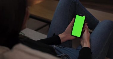 Yong Btunette denen kadın oturma odasında kanepeye oturmuş elinde yeşil maket ekranlı akıllı bir cep telefonu tutuyor. İnternet 'te gezinen kız resimleri gözlemliyor.