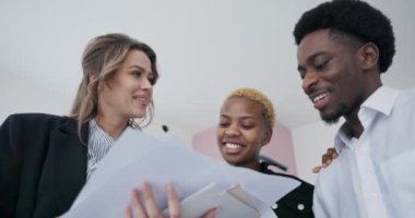 Yakın çekim Afrikalı çift ve emlakçı arasındaki animasyon sohbetine odaklanıyor. Yakında evde olacakları yerin mimari planlarını titizlikle analiz ediyorlar..