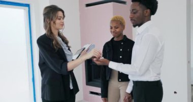 Yakın çekim anahtarın değişimine odaklanıyor. Sarışın emlakçı kadın ve Afrikalı çift arasındaki neşe ve minnettarlığı gözler önüne seriyor..