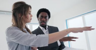 Kendine güvenen Afrikalı gayrimenkul uzmanları geniş pencereli lüks çatı katları müşterilere nefes kesici şehir manzarası sunan sofistike sarışın kadınlar kendilerini hayranlıkla seyrediyorlar..