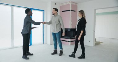 Afrikalı emlakçı kontratı elinde tutuyor. Kameraya bakarken yüzünde kocaman bir gülümseme var. Başparmak işareti var..