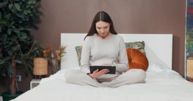 Elinde bir tablet ve yüzünde bir gülümseme ile, nilüfer çiçekli hamile bir kadın, kıymetli bir ufaklığın gelişini beklerken gelen huzur ve sevgiyi yayıyor..