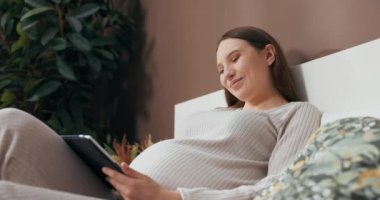 Rüya gibi, şık ve rahat kıyafetler giymiş hamile bir kadını cezbediyor. Yatakta oturuyor, elinde bir tablet tutuyor ve resimlere hayranlıkla bakıyor..