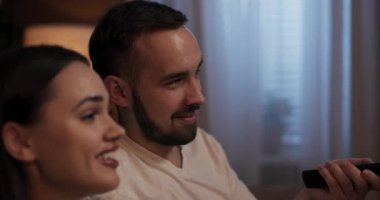 Konforlu oturma odasında genç bir kadın ve erkek rahat bir şekilde kanepede oturup TV 'de film seyrediyor, gözleri perdeye yapışıktı. Ara sıra, kanalı değiştirip izleyecek bir şey arıyorlar..
