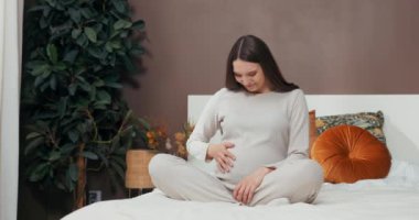 Kısa saçlı hamile bir kadın büyüyen karnına dokunurken neşe ve merakla ışıldayarak içinde büyüyen hayata hayret eder..