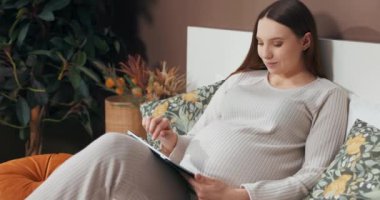 Hamile bir kadının elinde tablet tutarken, resimlerini aşırırken ve dikkatle incelerken yakın plan bir çekim..