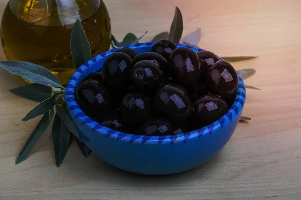 Black olives in the bowl with oil and leaves
