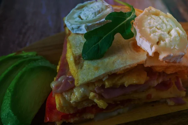 sandwich of tomato, tortilla, ham and goat cheese with avocado on a wooden board