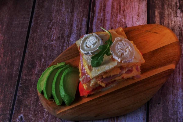 sandwich of tomato, tortilla, ham and goat cheese with avocado on a wooden board