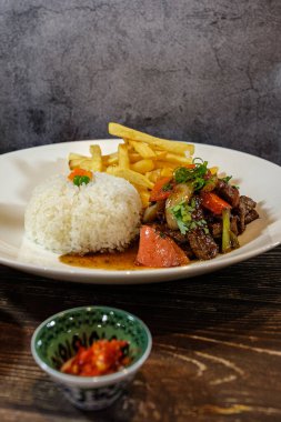 Lomo saltado, beyaz pirinç ve patates kızartması, ahşap masada servis edilir.