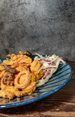 Kızarmış balık, kalamar ve soğanla birlikte bir tabak ve salata.