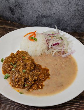 Tavuk ve biftekli beyaz fasulye, pirinç ve kırmızı soğanla servis edilir.